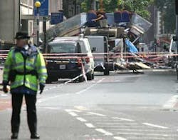 A police officer stands guard at the entrance to Eversholt Street after a bus, background, was bombed in Russel Square, Central London, Thursday, July 7, 2005. Near simultaneous explosions rocked at least five London subway stations and ripped apart a dou