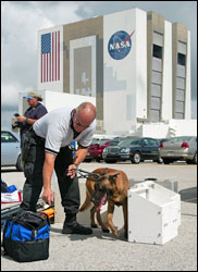 A NASA security officer inspects photographers' gear with a explosives sniffing dog at the Kennedy Space Center in Cape Canaveral, Fla., on Tuesday, July 12, 2005. The Space Shuttle Discovery is scheduled for launch today.