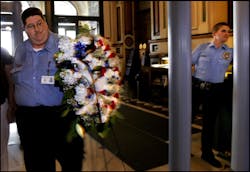 Illinois Secretary of State security guard Carl Faust, left, carries a wreath of flowers around the metal detector at the north entrance of the Illinois state Capitol in Springfield, Ill. He is joined by Mitch White of ELA Security, who is working the fac