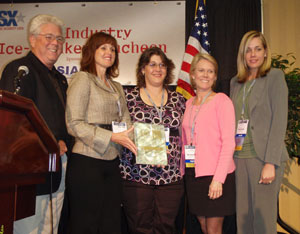 Frank Burke (NBFAA) presented the NBFAA First Line of Defense Award to Brink's Home Security for its protection of Julie Bender's life. Bender is pictured (right of center) with Brink's monitoring station operator Diana (center). Julie said Diana is her '