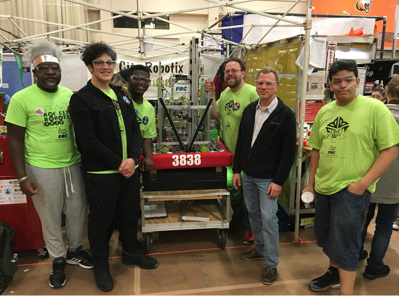 Paul Wisotzke, manager, test and validation, LenelS2 (black jacket, second from right), is one of several company mentors supporting Pathways in Technology (P-TECH) in Rochester, N.Y. The international six-year program helps prepare students for IT-based careers in security and other industries. A LenelS2 grant enabled a high school team to build a robot in a recent regional P-TECH competition.