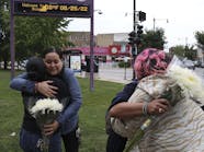 Following a shooting that left four people injured at an ice cream shop across the street from Carl Schurz High School, Sandra Acebedo, left, hugs and greets Norma Rios Sierra, as Juliet De Jesus Alejandre, right, back to camera, is greeted and hugged by a parent of high school student Monica Espinoza, who was handing out flowers to students, parents and staff on Thursday, Aug. 25, 2022. .