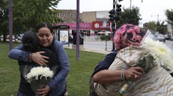 Following a shooting that left four people injured at an ice cream shop across the street from Carl Schurz High School, Sandra Acebedo, left, hugs and greets Norma Rios Sierra, as Juliet De Jesus Alejandre, right, back to camera, is greeted and hugged by a parent of high school student Monica Espinoza, who was handing out flowers to students, parents and staff on Thursday, Aug. 25, 2022. .